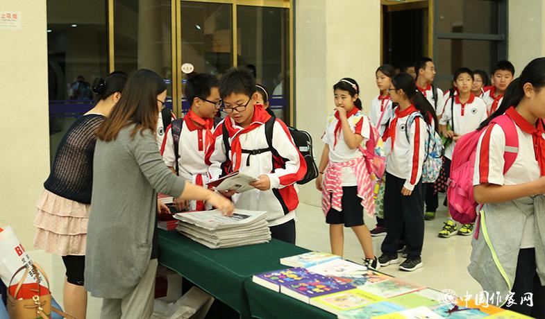 參加頒獎(jiǎng)典禮的學(xué)生排隊(duì)入場，工作人員為他們分發(fā)當(dāng)天的《文藝報(bào)》兒獎(jiǎng)特刊